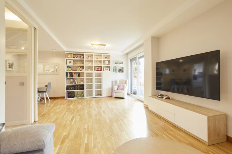 Salón con estantería de libros infantiles, sillón blanco y mueble de televisión