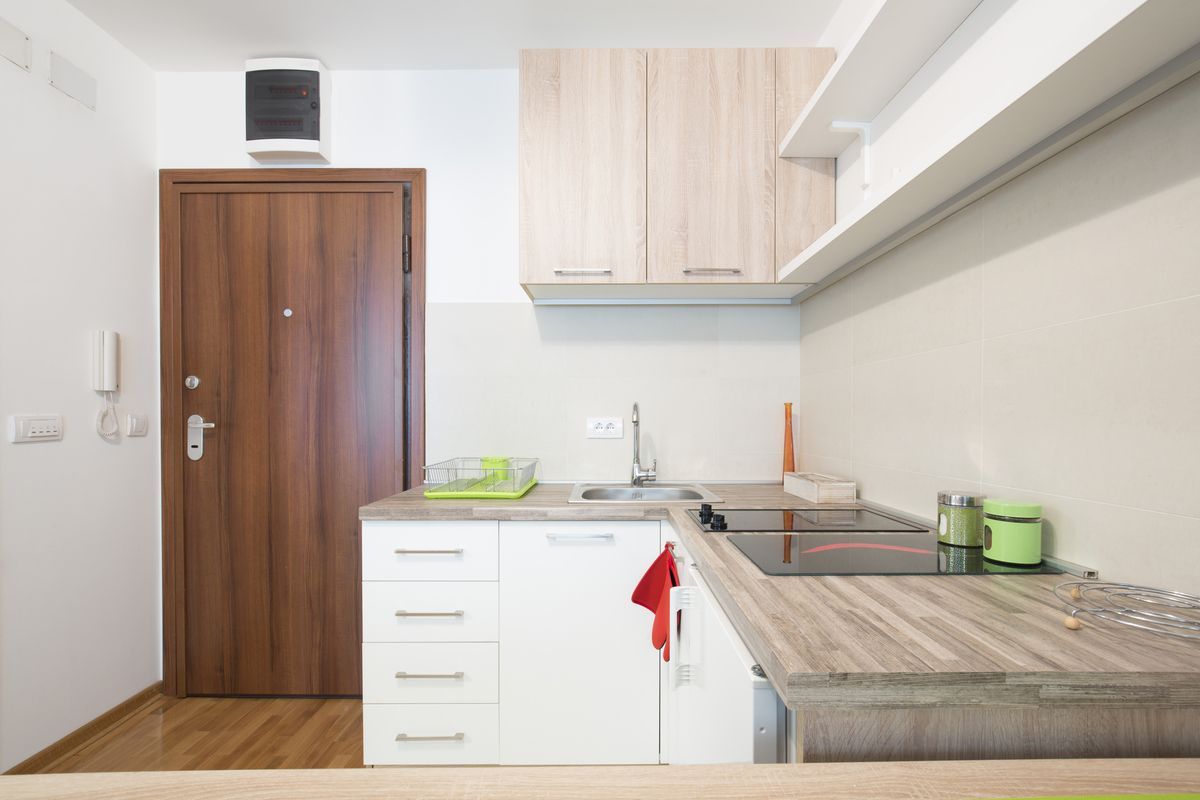 Cocina pequeña en L con frentes blancos y encimera de madera junto a la puerta de entrada