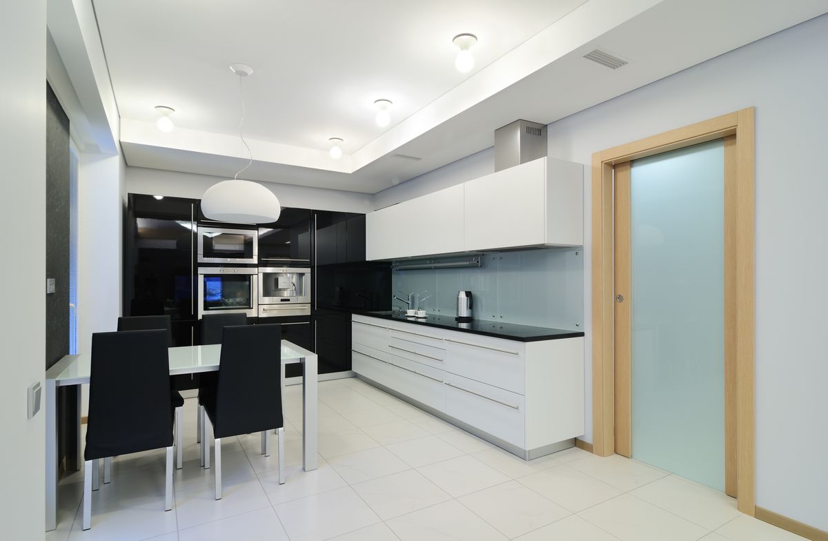 Cocina blanca en línea con muebles negros y comedor integrado en la misma estancia